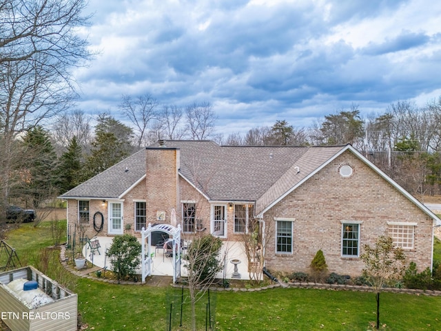 single story home with a shingled roof, a patio, a chimney, a front lawn, and brick siding