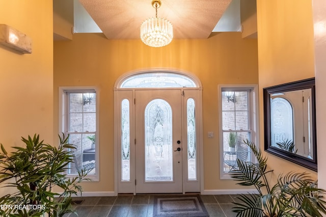 foyer featuring a chandelier, dark tile patterned floors, and baseboards