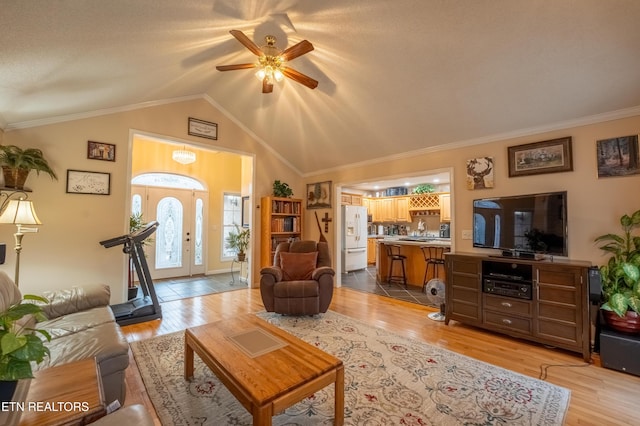 living area with light wood-type flooring, ornamental molding, and vaulted ceiling