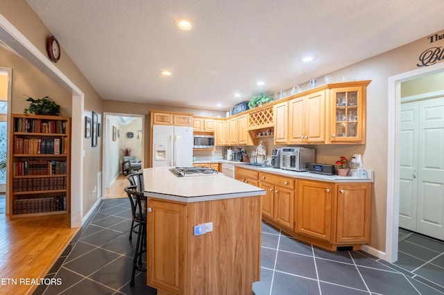 kitchen featuring a kitchen island, stainless steel microwave, a breakfast bar, dark tile patterned floors, and white fridge with ice dispenser