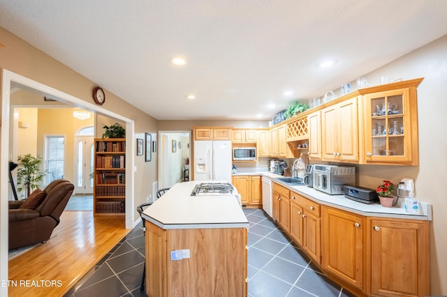 kitchen featuring light countertops, glass insert cabinets, a kitchen island, white appliances, and dark tile patterned floors