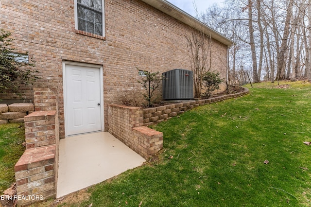 view of exterior entry featuring a lawn and brick siding