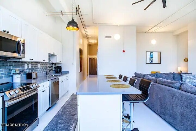 kitchen with a sink, backsplash, a kitchen bar, stainless steel appliances, and white cabinets