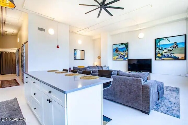 kitchen with visible vents, a kitchen island, a ceiling fan, white cabinetry, and open floor plan