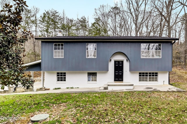 split foyer home with brick siding, a patio, a chimney, and a front lawn