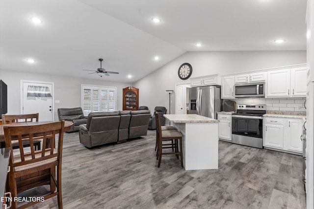 kitchen with a center island, a breakfast bar area, light countertops, lofted ceiling, and appliances with stainless steel finishes