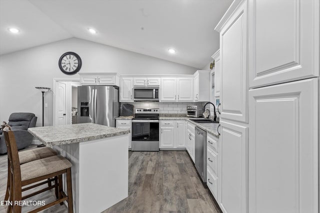 kitchen with vaulted ceiling, decorative backsplash, stainless steel appliances, dark wood-style floors, and white cabinetry