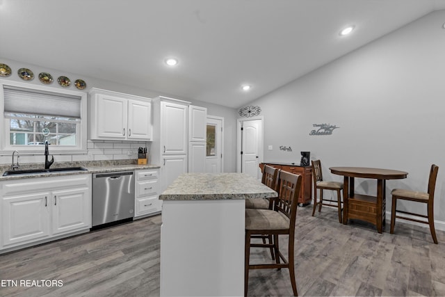 kitchen featuring a sink, a kitchen breakfast bar, lofted ceiling, and stainless steel dishwasher