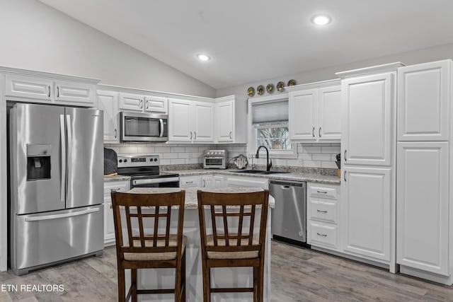 kitchen with a sink, vaulted ceiling, appliances with stainless steel finishes, white cabinetry, and tasteful backsplash