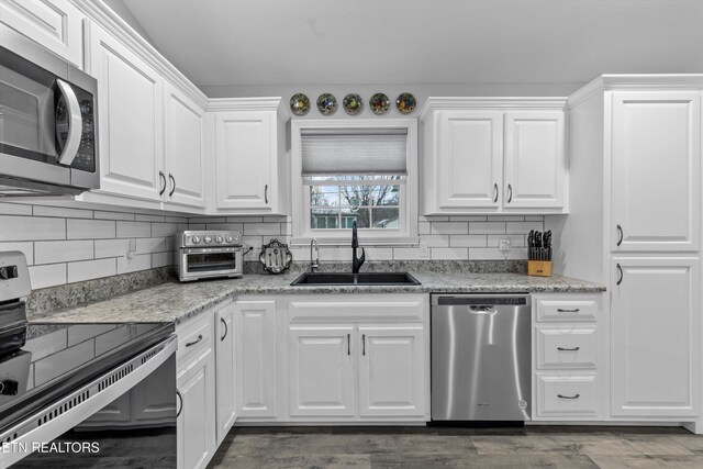 kitchen featuring tasteful backsplash, appliances with stainless steel finishes, dark wood-style floors, white cabinets, and a sink