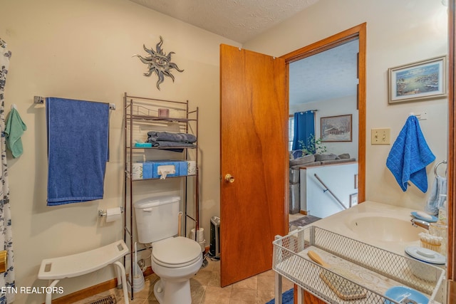 bathroom with a textured ceiling, tile patterned floors, toilet, and a sink