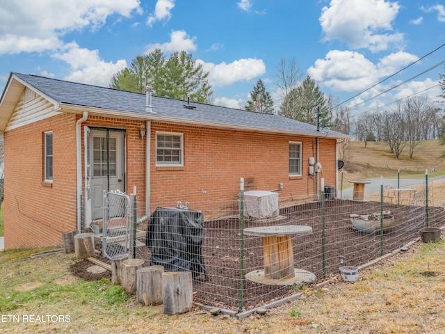 rear view of property featuring central AC unit, brick siding, and roof with shingles