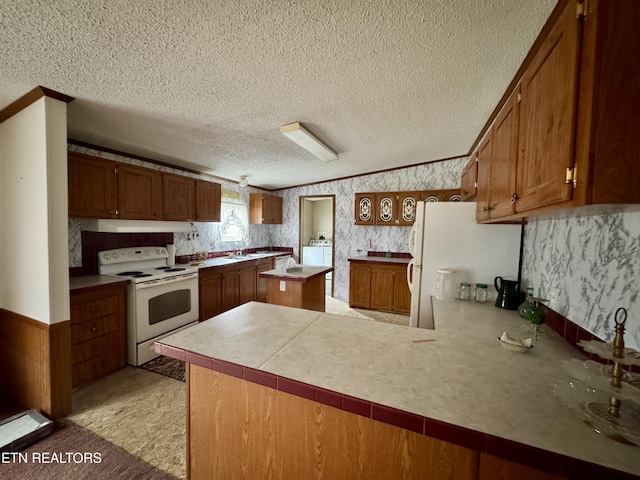 kitchen with a textured ceiling, a peninsula, white appliances, brown cabinetry, and wallpapered walls