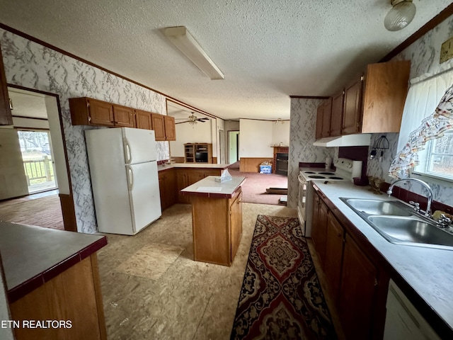 kitchen featuring a sink, a textured ceiling, white appliances, a peninsula, and wallpapered walls