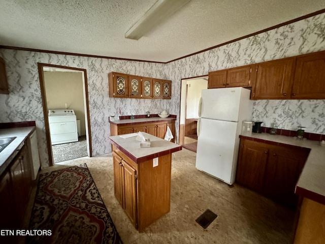 kitchen with washer / dryer, wallpapered walls, brown cabinetry, freestanding refrigerator, and a textured ceiling