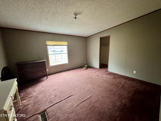 unfurnished bedroom with a textured ceiling, carpet flooring, visible vents, vaulted ceiling, and crown molding