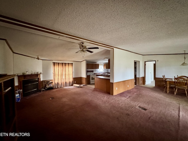 unfurnished living room with a textured ceiling, a wainscoted wall, wood walls, a fireplace, and a ceiling fan