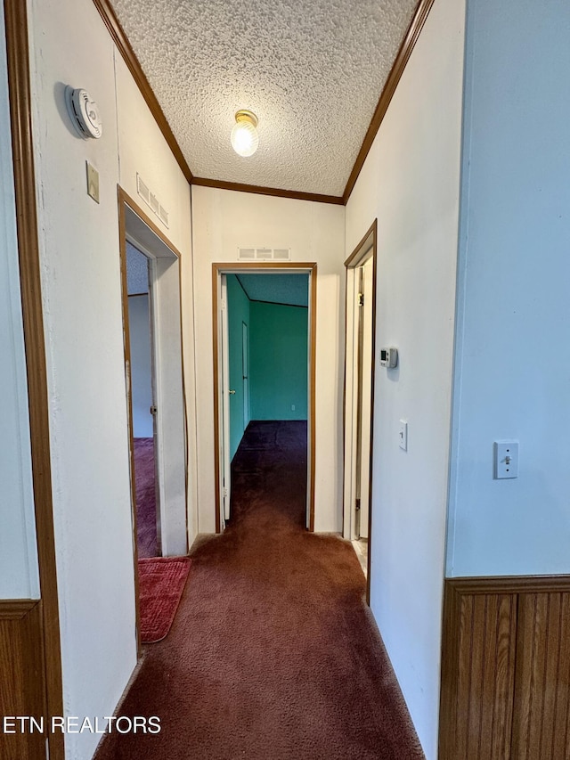 hall with ornamental molding, a textured ceiling, visible vents, and carpet