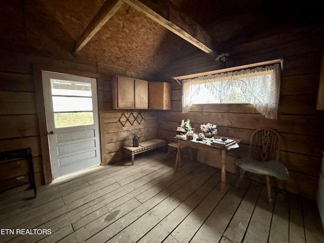 dining room with wood-type flooring, vaulted ceiling, wooden walls, and plenty of natural light