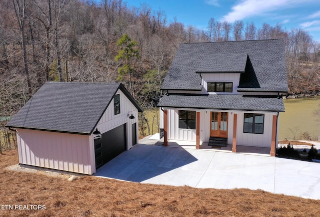 modern inspired farmhouse featuring a garage, an outdoor structure, french doors, roof with shingles, and board and batten siding