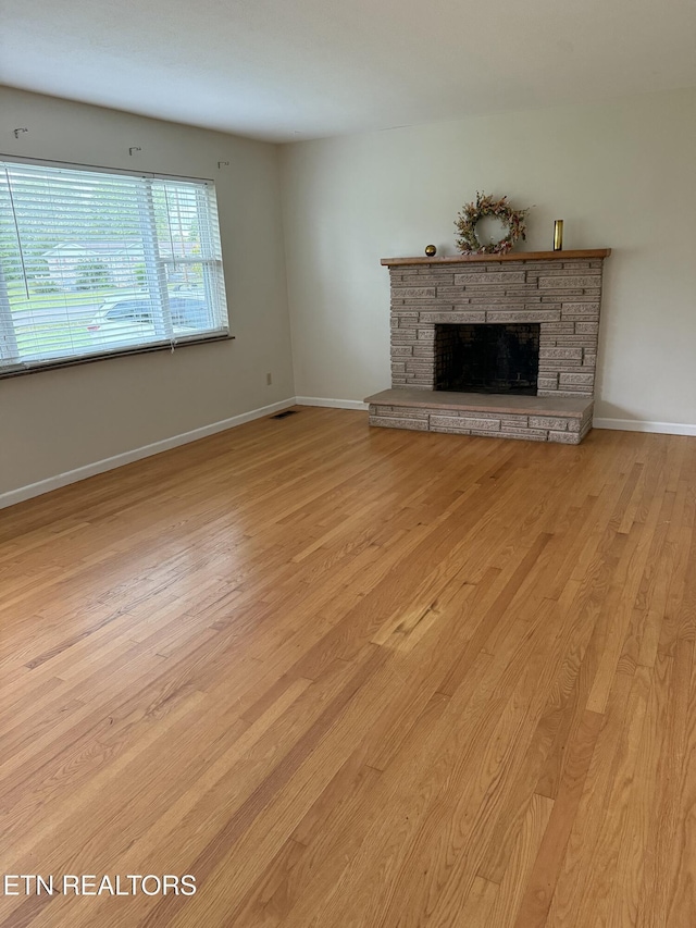 unfurnished living room with baseboards, a fireplace, visible vents, and light wood finished floors