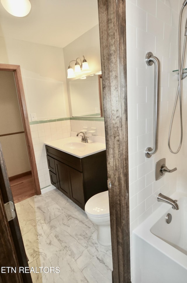 full bath featuring toilet, vanity, marble finish floor, shower / bathtub combination, and tile walls