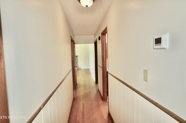 corridor with a wainscoted wall and light wood finished floors