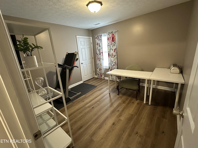 home office with visible vents, a textured ceiling, baseboards, and wood finished floors