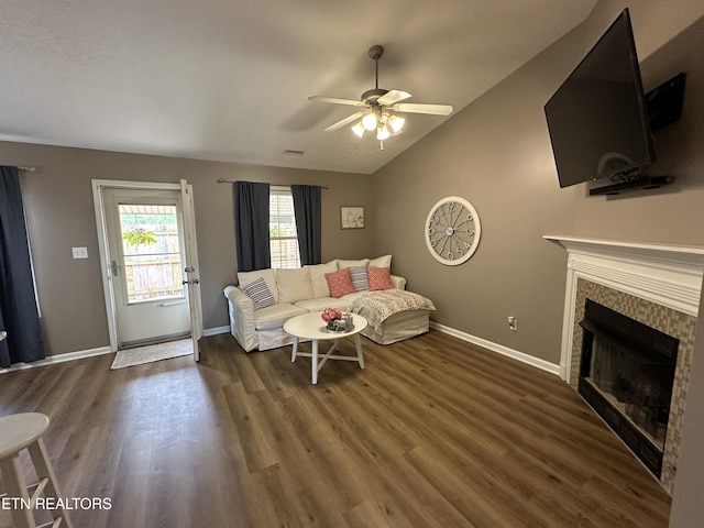 living area with lofted ceiling, a tiled fireplace, a ceiling fan, wood finished floors, and baseboards