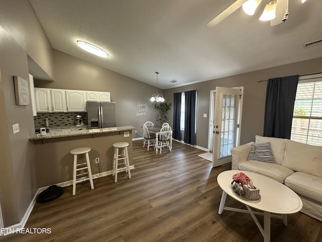 living room with dark wood-style floors, lofted ceiling, visible vents, baseboards, and ceiling fan with notable chandelier