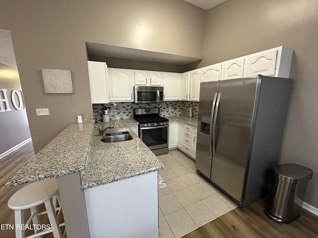 kitchen with light stone counters, stainless steel appliances, a peninsula, a sink, and tasteful backsplash