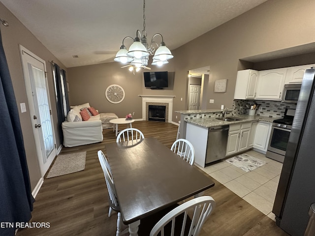 kitchen featuring a fireplace, a sink, vaulted ceiling, open floor plan, and appliances with stainless steel finishes