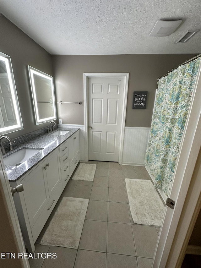 full bath featuring tile patterned flooring, a wainscoted wall, a sink, and visible vents