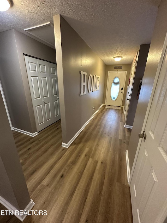 hall with a textured ceiling, baseboards, and dark wood-type flooring