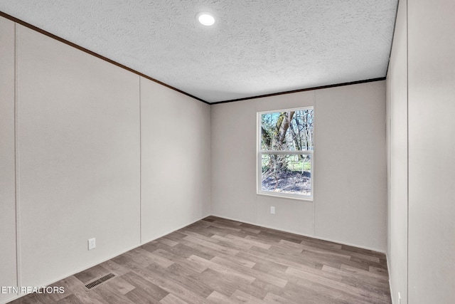 empty room with a textured ceiling, ornamental molding, wood finished floors, and visible vents