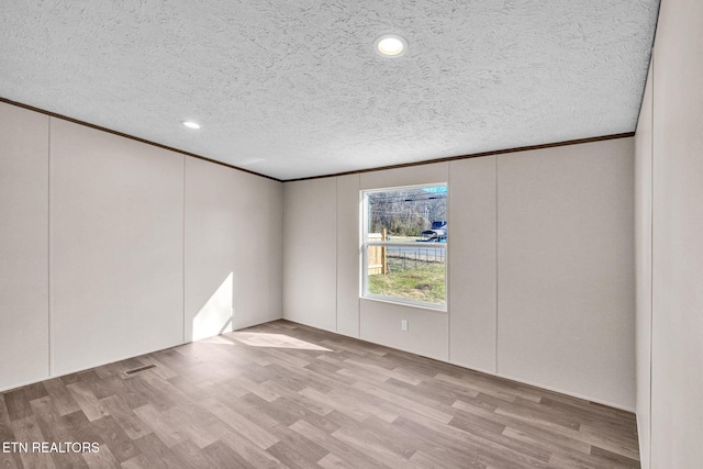 unfurnished room with a textured ceiling, a decorative wall, wood finished floors, visible vents, and crown molding