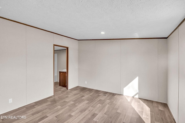 empty room with light wood-type flooring, ornamental molding, and a textured ceiling