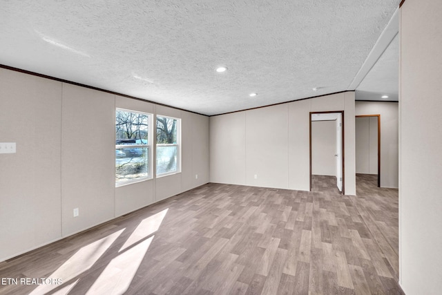 empty room featuring a textured ceiling, crown molding, and light wood-style floors