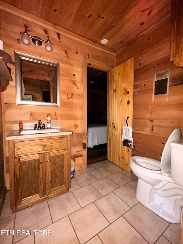 ensuite bathroom with wooden walls, toilet, wood ceiling, tile patterned floors, and vanity