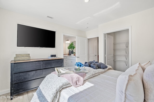 bedroom with visible vents, ensuite bath, baseboards, and wood finished floors