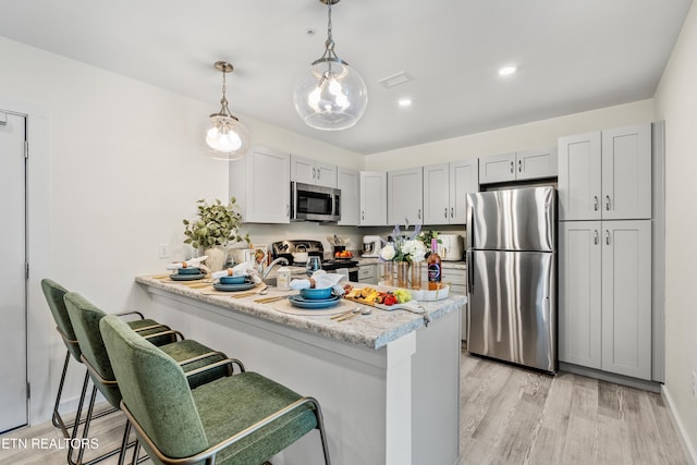 kitchen with a breakfast bar area, a peninsula, light wood-style flooring, appliances with stainless steel finishes, and decorative light fixtures