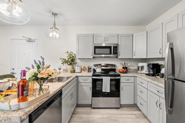 kitchen with gray cabinets, hanging light fixtures, light countertops, light wood-style floors, and appliances with stainless steel finishes