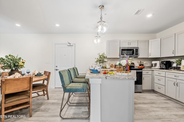 kitchen featuring visible vents, decorative light fixtures, a breakfast bar area, light wood-style flooring, and appliances with stainless steel finishes