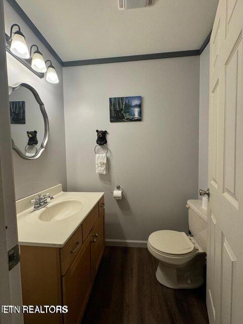 half bath featuring ornamental molding, vanity, toilet, and wood finished floors