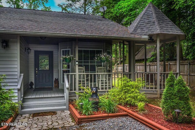 doorway to property featuring fence and roof with shingles