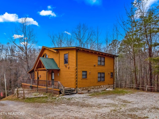 rustic home featuring driveway, metal roof, fence, and a deck