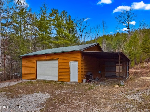 detached garage featuring a carport, a wooded view, and dirt driveway