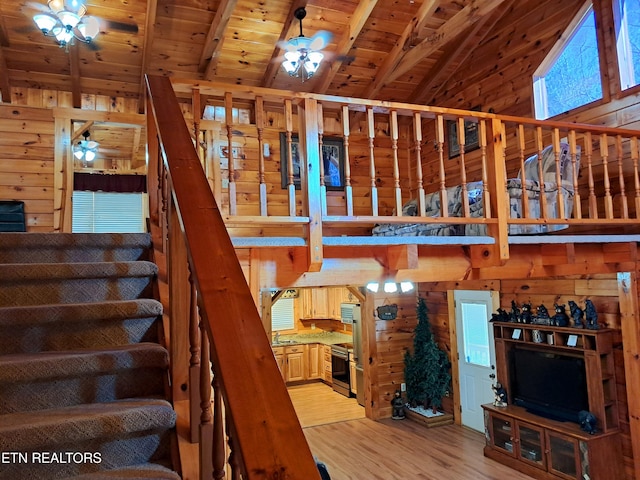 stairway with wooden walls, a ceiling fan, lofted ceiling with beams, wooden ceiling, and wood finished floors