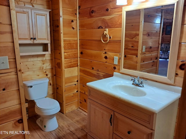 half bathroom featuring vanity, wood walls, wood finished floors, and toilet