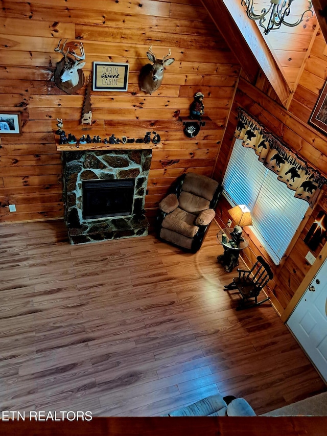 unfurnished living room featuring lofted ceiling, wood walls, wood finished floors, and a stone fireplace